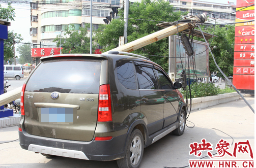 一根线杆从根部折断，压倒在一辆棕色私家车上