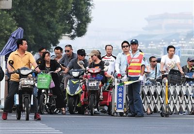 　昨日，长安街西单路口，交通协管员指挥人们在伸缩门后等待绿灯，一名黄衣男子骑电动车抢行。新京报记者 尹亚飞 摄