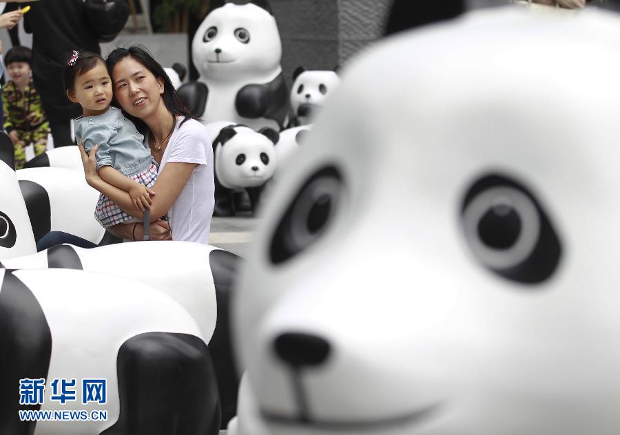 6月2日，一位家长带着孩子在上海街头和大熊猫模型合影。